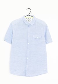 Camicetta blu a maniche corte con tessuto testurizzato, taschino sul petto e colletto interno a fantasia. Appesa a un gancio nero.