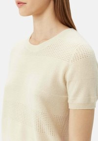 Ljusbeige kortärmad tröja med en blandning av strukturerade ränder och öppna vävmönster, med rund halsringning och mjukt tyg.