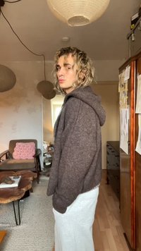 Cozy brown zip-up hoodie with a hood, textured fabric. Paired with a white, knee-length skirt. Soft lighting and wooden furniture in background.