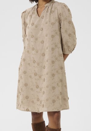 Hellbeiges knielanges Kleid mit 3D-Blumenstickerei, 3/4-Puffärmeln und kleinem V-Ausschnitt, getragen mit braunen Stiefeln bis zur Mitte der Wade.