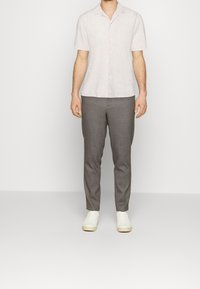 Chemise en lin gris clair à manches courtes avec un col, bouton devant ; associée à un pantalon taillé gris foncé et des baskets blanches. Design minimaliste.