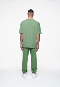 Zelené oversize tričko z bavlny a odpovídající tepláky. Oblečení má pohodlný střih a je doplněno bílými teniskami.