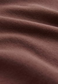 Tessuto marrone con una texture liscia e morbida, che presenta pieghe delicate e dinamiche sulla superficie. La vista ravvicinata enfatizza la ricchezza del materiale.