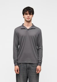 Polo à manches longues gris avec texture côtelée, col à revers et poignets ajustés, associé à un jean en denim foncé.