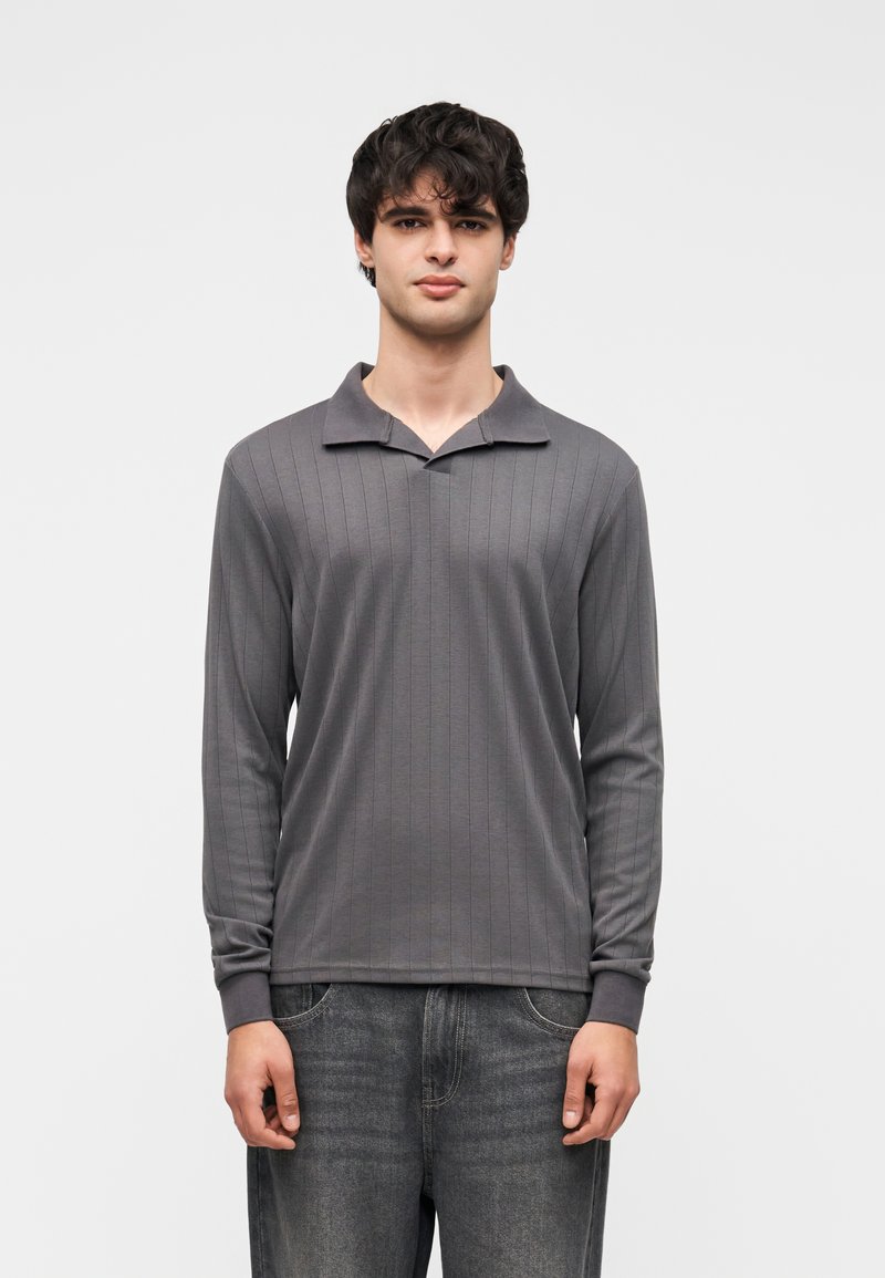 Polo à manches longues gris avec texture côtelée, col à revers et poignets ajustés, associé à un jean en denim foncé.