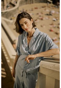 Camicia di cotone azzurro chiaro con colletto e maniche corte, abbinata a pantaloni ampi dello stesso colore. Tessuto liscio, design casual, vestibilità rilassata.