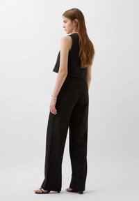 Černý dvoudílný outfit se skládá z krátkého bezramínkového topu a širokých kalhot. Materiál vypadá texturovaně a má hladký povrch.