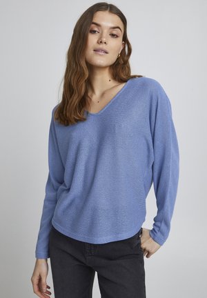 Top de punto de color azul claro, de manga larga, con escote en V y hombros caídos, combinado con jeans oscuros. Textura suave y ajuste relajado.