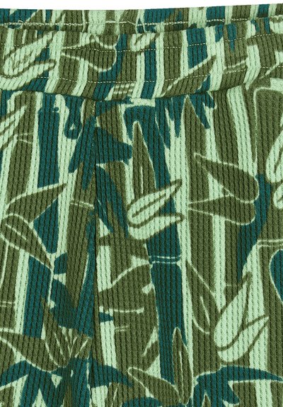 Groen geribd stof met een patroon van donker groene en blauwe botanische bladeren op een lichtgroene achtergrond. Detail van de elastische tailleband zichtbaar.