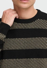 Black and beige striped knit sweater with a ribbed crew neckline. Features textured fabric alternating between solid and patterned stripes.