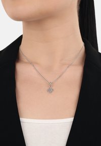 Pendente a forma di albero della vita in argento su una delicata catena, indossato sopra un blazer nero e una maglietta bianca, che mette in evidenza i dettagli di design intricati.