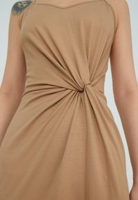 Robe sans manches kaki avec un détail twisté à la taille, confectionnée dans un tissu lisse, présentant des plis drapés et une coupe décontractée.