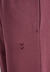 Bordowe spodnie sportowe z miękkiego materiału, z subtelnym tłoczonym logo w kształcie szewrona po boku oraz bocznymi kieszeniami.