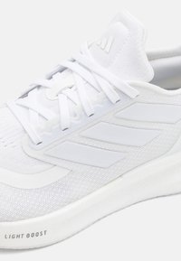 Zapatilla deportiva blanca con parte superior de punto, tres acentos de franjas blancas, suela texturizada y la marca "LIGHT BOOST" en el lateral.