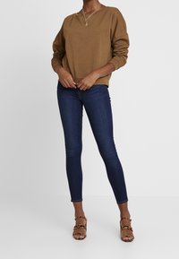 Sudadera marrón de corte relajado, combinada con jeans ajustados de color azul oscuro y tacones de tiras con estampado de leopardo. Cuello simple y tejido texturizado.