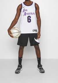 Maglia da basket bianca con "Los Angeles" e numero "6" in viola, abbinata a pantaloni corti neri, calze Nike nere e scarpe Nike grigie.