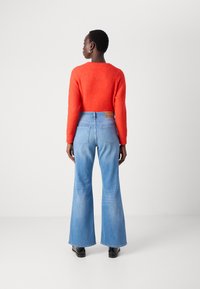 Rød, strukturert genser kombinert med lyseblå, utsvingte jeans med et lærmerke. Jeansene har et klassisk fem-lommes design.