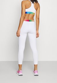 Bílé sportovní legíny a odpovídající sportovní podprsenka s vícbarevnými elastickými pásky s nápisem "Calvin Klein." Lehký, na tělo přiléhavý materiál.