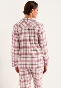 Geruite pyjama-set in het wit met roze en bordeauxrode ruitpatronen. Zachte stof, lange mouwen, knoopsluiting en bijpassende broeken.