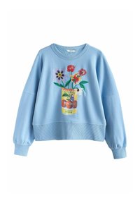 Lichtblauwe sweater met geborduurde kleurrijke bloemen op een gele kan met het opschrift "Sun Bird Peaches" gedrukt op de voorkant.