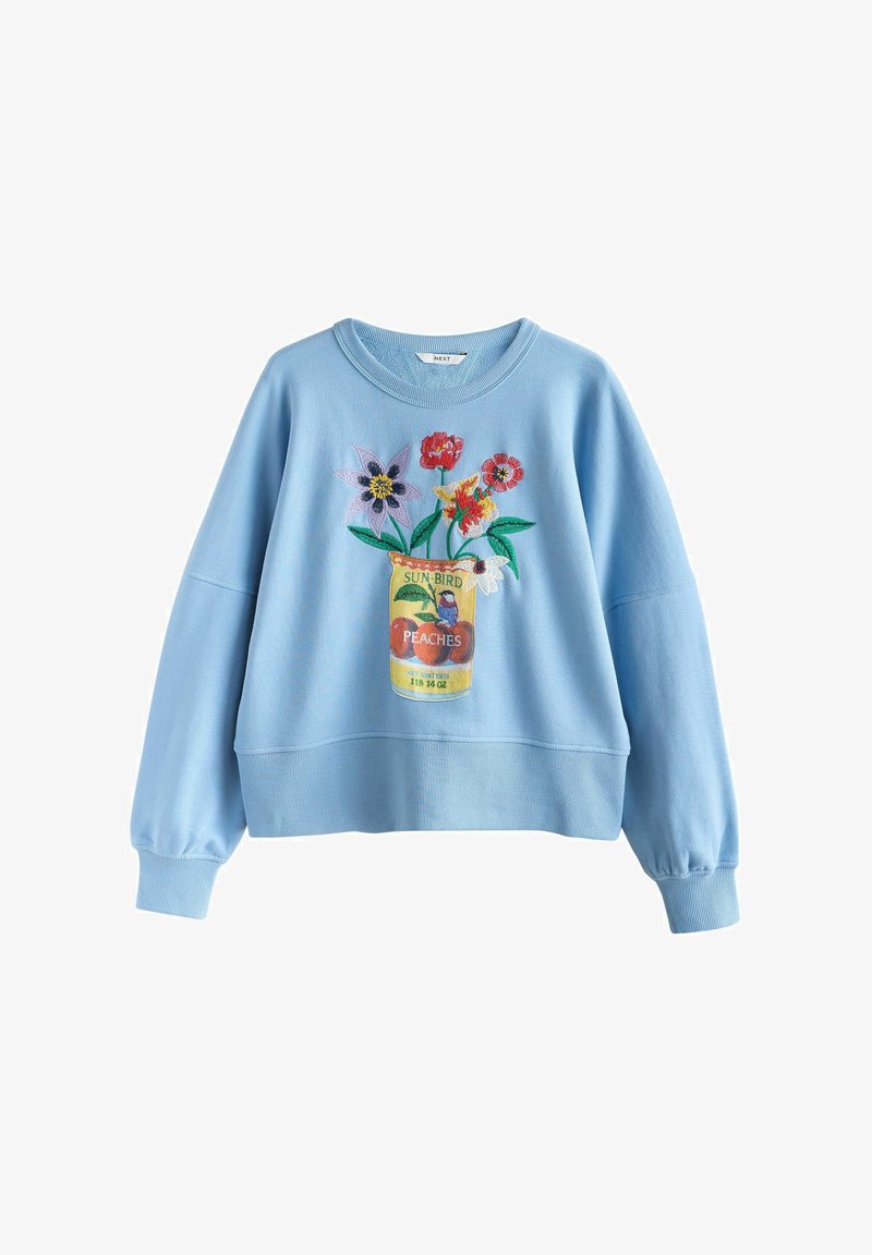Lichtblauwe sweater met geborduurde kleurrijke bloemen op een gele kan met het opschrift "Sun Bird Peaches" gedrukt op de voorkant.