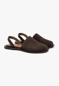 Bruine suède slingback-schoenen met een gladde afwerking, ronde neus en een platte zwarte zool. Open achterkant ontwerp met minimale hardware-details.