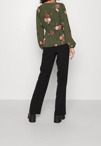 Zielona bluzka typu peplum z długimi rękawami, z wzorem różowych i żółtych kwiatów, zestawiona z czarnymi spodniami o wysokim stanie i masywnymi czarnymi butami.