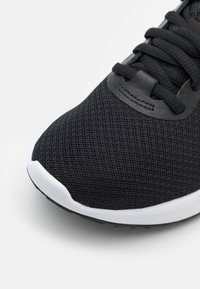 Zapatilla atlética de malla negra con cordones negros y suela blanca, mostrando un primer plano de la punta y la parte superior frontal.