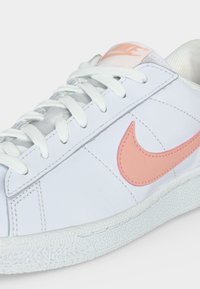 Άσπρο sneaker χαμηλού προφίλ με ανοιχτό ροζ λογότυπο Nike και σήμα στη γλώσσα, λευκά κορδόνια και υφασμένη ελαστική σόλα.