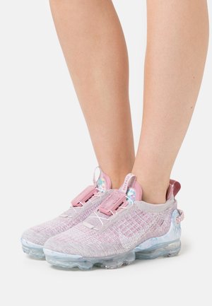 Paire de baskets tricotées rose pâle et lavande avec semelles translucides portées pieds nus sur fond blanc.