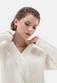 Strickpullover in cremigem Weiß, mit V-Ausschnitt, geripptem Design und langen Ärmeln. Hervorzuheben ist der weiche und leichte Stoff.