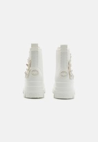 Witte enkellaarzen met bloemaccenten, gestructureerd materiaal en chunky zolen. Bevat logo-detail op de hak en achterste trekbands.