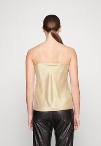 Camisola in satin color oro chiaro con spalline sottili e regolabili e schiena dritta, abbinata a pantaloni in pelle nera con cuciture decorative.