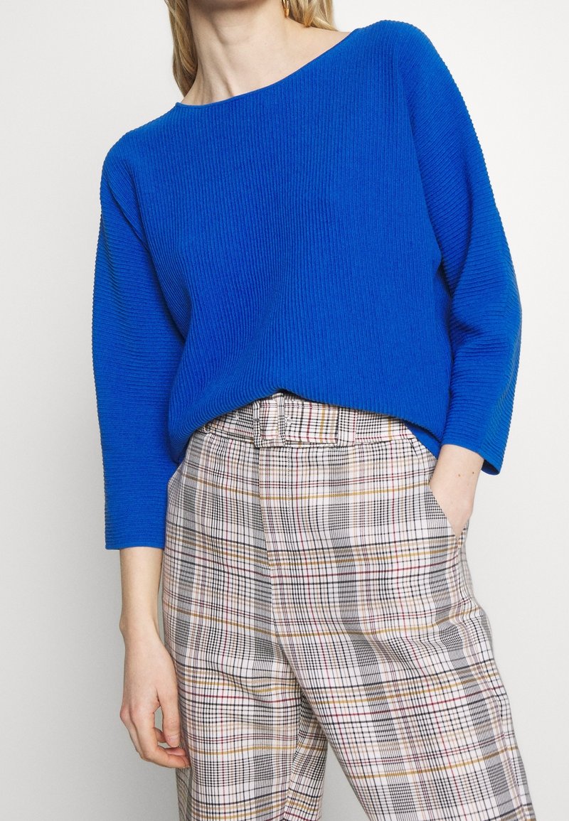 Blå ribbad tröja med bred båtkrage, i kombination med rutiga beige och bruna högmidjade byxor med varierande rutig mönster.