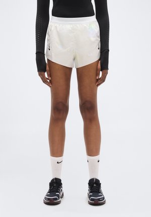 Pantaloncini da corsa bianchi, leggeri e riflettenti, con perforazioni laterali, abbinati a maniche lunghe nere, scarpe da ginnastica nere e bianche e calze fino al ginocchio.