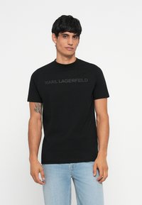 Črna bombažna majica s kratkimi rokavi in krožnim izrezom. Logo "KARL LAGERFELD" v toniranem tisku na prsih.