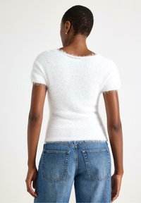 Hvid, fluffy kortærmet sweater med blød tekstur, rund halsudskæring og let figursyet design, parret med lyseblå denimjeans.