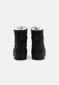 Botas de tobillo de ante negro con un eje acolchado, forro de felpa blanca y suela de goma negra texturizada. Presenta un logo en la parte posterior.
