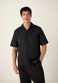Short-sleeve black shirt with a textured pattern, button-up front, and a relaxed fit, paired with dark trousers.