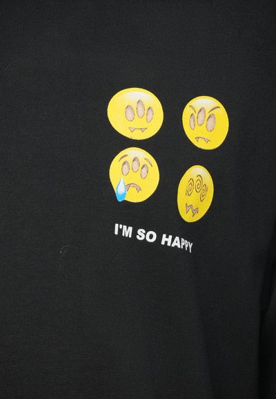 Sort t-shirt med fire gule emotikoner med forskellige udtryk; teksten "JEG ER SÅ GLAD" trykt i hvidt under designet.