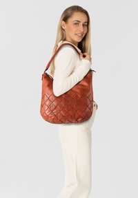 Sac en cuir brun avec un motif de losanges matelassé, doté d'une bandoulière tressée et d'une forme douce et décontractée.