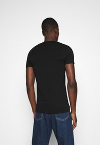 Schwarz Baumwoll-T-Shirt mit rundem Ausschnitt und kurzen Ärmeln, taillierte Passform, glatte Textur, kombiniert mit blauen Jeans.