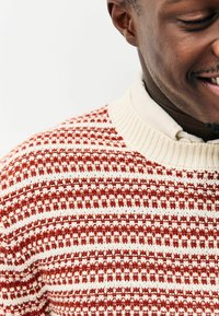 Red and white patterned knit sweater with a ribbed neckline, featuring horizontal stripes and textured weaving. Cotton blend material.