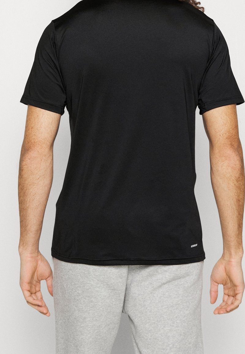 Camiseta deportiva negra de tejido suave, con mangas cortas y un escote redondeado, mostrada desde la parte de atrás con una cinturilla gris en la parte inferior.