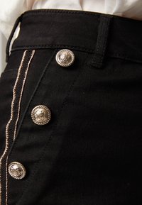 Zwarte denim rok met vijf decoratieve zilveren knopen aan de voorkant, elk met een gevlochten ontwerp en contrasterende stiksels.