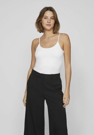 Witte tanktop met dunne bandjes, gecombineerd met hoge taille zwarte wijde broek. Smooth textuur met minimale detailing. Effen achtergrond.