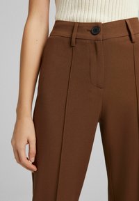 Bruna skräddarsydda byxor med en slät yta, enkel knappstängning och framfickor i en smal, rak design.