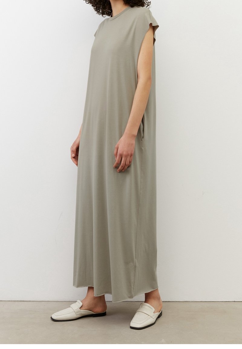 Długa, luźna sukienka z miękkiego, lekkiego zielonego materiału. Posiada rękawki typu cap, boczne kieszenie i okrągły dekolt. Noszona z białymi klapkami.