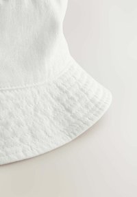 Weißer Baumwoll-Eimerhut mit einem breiten, runden Rand. Die Textur ist glatt mit sichtbaren Nähten entlang der Kante.