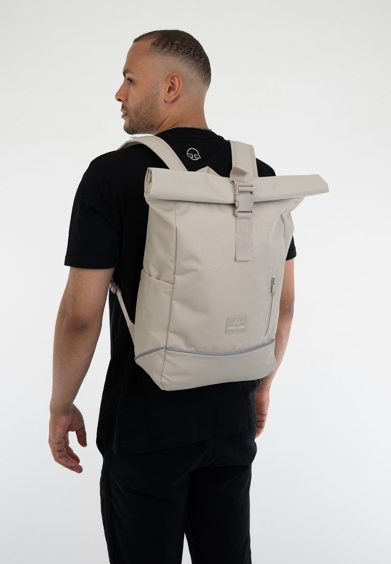 Beige, felhajtható hátizsák, letisztult dizájnnal, szövet anyagból készült, elülső cipzáras zsebbel és állítható pántokkal. Az elején logó található.